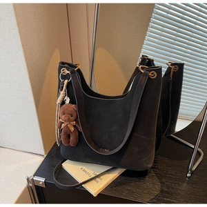 Detail of black suede tote bag with metal ring strap and cute bear plush charm