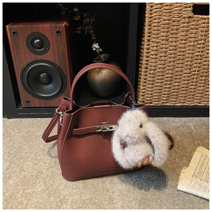 Detail of reddish-brown bucket bag with leather strap and plush rabbit charm accessory
