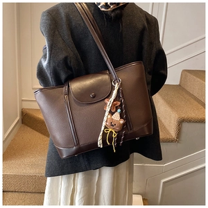 Brown large capacity tote bag worn with black blazer and stylish teddy bear charm