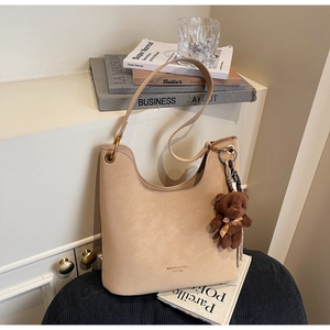 Detail einer beige Hobo-Tasche mit matter Textur und braunem Plüschbär-Anhänger