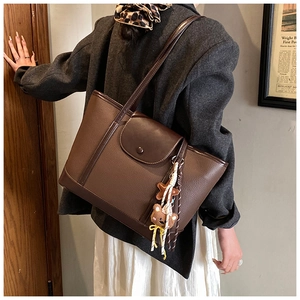 Detail of coffee brown tote bag in lychee pattern leather with a cute plush bear pendant