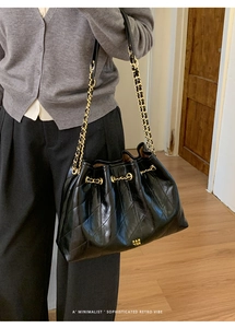Detailansicht der schwarzen gesteppten Beuteltasche mit goldener Kette am Modell