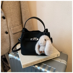 Close-up of black lychee grain leather bucket bag with silver lock and plush bunny charm