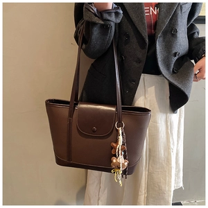 Detail of dark brown leather tote bag with semi-circular flap and plush bear charm