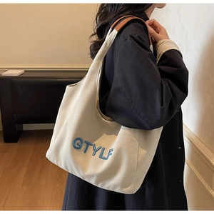 Detail view of canvas tote featuring blue GTYLF embroidery and brown leather handles