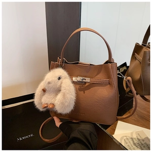 Detail of a brown bucket bag with a silver turn-lock and a white rabbit charm decor