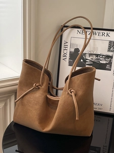 Brown suede tote bag with knot handle detail on a modern reflective studio setting