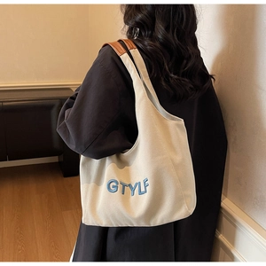 Detail of the minimalist canvas tote bag featuring blue GTYLF embroidery and brown leather strap