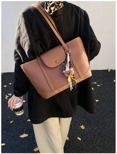Detailed view of a brown leather tote bag featuring a cute plush bear charm and magnetic flap