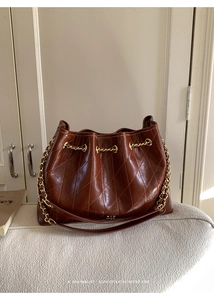 Nahaufnahme braune Stepptasche aus Leder mit goldener Kette auf einem Polsterhocker