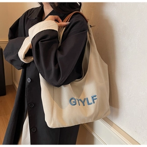 Detail of large canvas tote bag with blue letter embroidery and brown leather handles