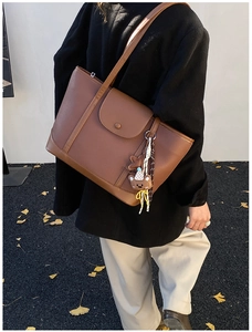 Detailed close-up of a large brown tote bag with a bear charm and a magnetic front pocket