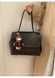 Dettaglio borsa tote retrò in pelle con ciondolo a orsetto, portata con trench beige