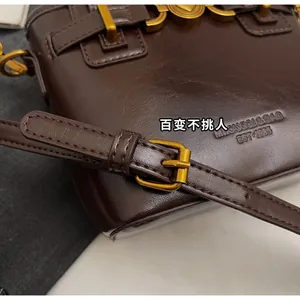 Detail of adjustable long shoulder strap with gold metal buckle on brown bucket bag