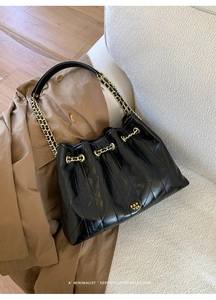 Detail einer schwarzen gesteppten Lackleder-Beuteltasche mit goldener Kette
