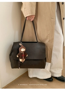 Dettaglio borsa tote in pelle marrone scuro con ciondolo a forma di orso e tracolla lunga