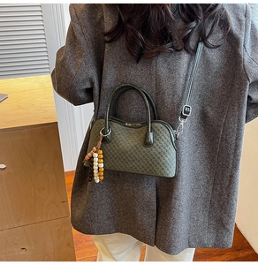 Détail du sac à main vert foncé tressé avec breloque en bois sur un blazer gris