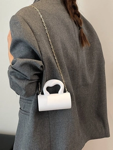 Sac cylindrique blanc en acrylique avec chaîne dorée porté sur une veste de blazer grise