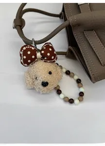 Close-up of beige plush dog charm with polka dot bow and beaded strap on brown leather bag