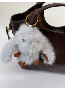 Close-up of a fluffy grey bunny plush pendant with gold metal ring and brown leather accents