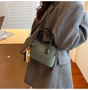 Detail of dark green woven texture bag with beaded charm and black leather shoulder strap