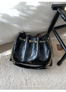 Detail einer schwarzen gesteppten Beuteltasche aus Leder mit goldener Kette auf Teppich