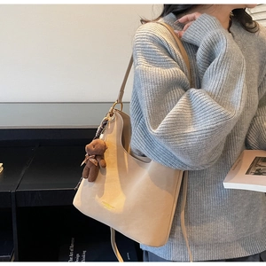 Seitenansicht der beigen Hobo-Schultertasche mit braunem Bärenanhänger und Goldlogo-Detail