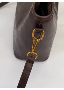 Close-up of retro bronze metal clasp and pebbled leather texture on dark brown bucket bag