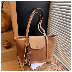 Detail of brown leather tote bag with flap closure and decorative star pendant accessory