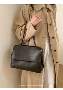 Dettaglio della grande borsa a tracolla in pelle retrò marrone scuro su un trench beige minimal