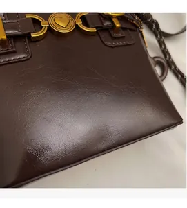 Detail of dark brown leather handbag with heart-shaped bronze buckle and embossed logo