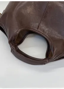 Detail of the deep brown leather handbag showing the curved top handle and neat stitching