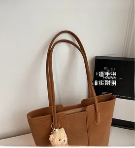Dettaglio della borsa tote in pelle scamosciata marrone con doppi manici e ciondolo a orsetto