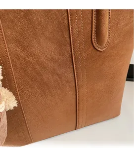 Dettaglio della borsa tote in pelle marrone con cuciture fini e ciondolo a forma di orso