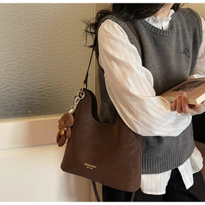 Detail der dunkelbraunen Wildleder-Hobo-Tasche mit Goldmarke und Plüschbär-Anhänger