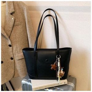Detail of black pebbled leather tote bag with cute bear charm on a silver suitcase
