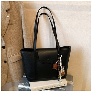 Detail of black pebbled leather tote bag with star and bear charms on a suitcase