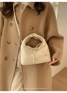 Detail of a beige faux leather bow handbag styled with a camel coat for a chic look