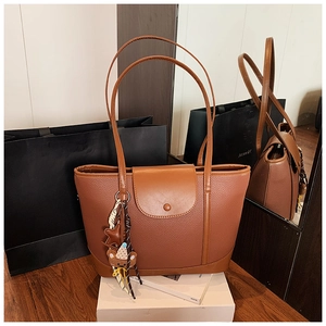 Detail of brown tote bag with leather texture, magnetic snap closure and bear pendant