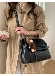 Dettaglio della borsa a tracolla retrò nera con ciondolo a forma di orso e trench beige