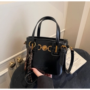 Detail of black leather handbag featuring golden heart buckle and leather tassel charm