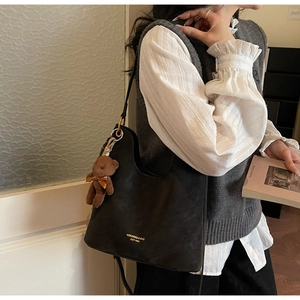 Detail der schwarzen matten Leder-Tote-Bag mit goldenem Logo und Plüschbär-Anhänger