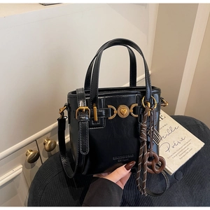 Detail of black handbag with gold heart lock and a cute brown pretzel charm decoration