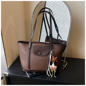 Close-up of brown pebbled leather tote bag with stylish bear charm and tassel detail