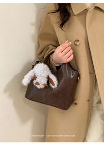 Close-up of retro dark brown leather bucket bag featuring a cute white plush bunny charm