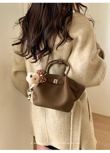 Close-up of coffee brown leather bucket bag with lychee texture and plush bear charm