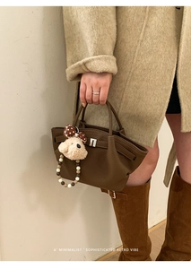 Detail view of dark brown leather bucket bag with silver lock and plush dog charm