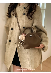 Brown lychee leather bucket bag with teddy bear charm shown on beige wool coat