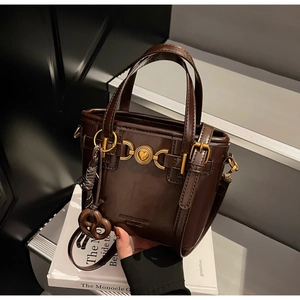 Close-up of dark brown leather handbag featuring a golden heart buckle and pretzel charm