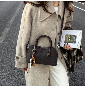 Detail of a dark brown checkered Boston bag featuring a vintage beaded charm and textured finish